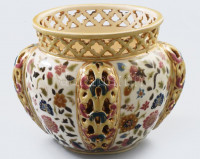 1880 körül, Zsolnay kaspó. Magastüzű színes mázakkal fedett porcelánfajansz. Oldalán kidomborodó szigetekben kettősfalú díszítés, pereme ismétlődő áttört minta. Jelzett: alján kobaltkék családi pecsét. Repedezett mázzal,